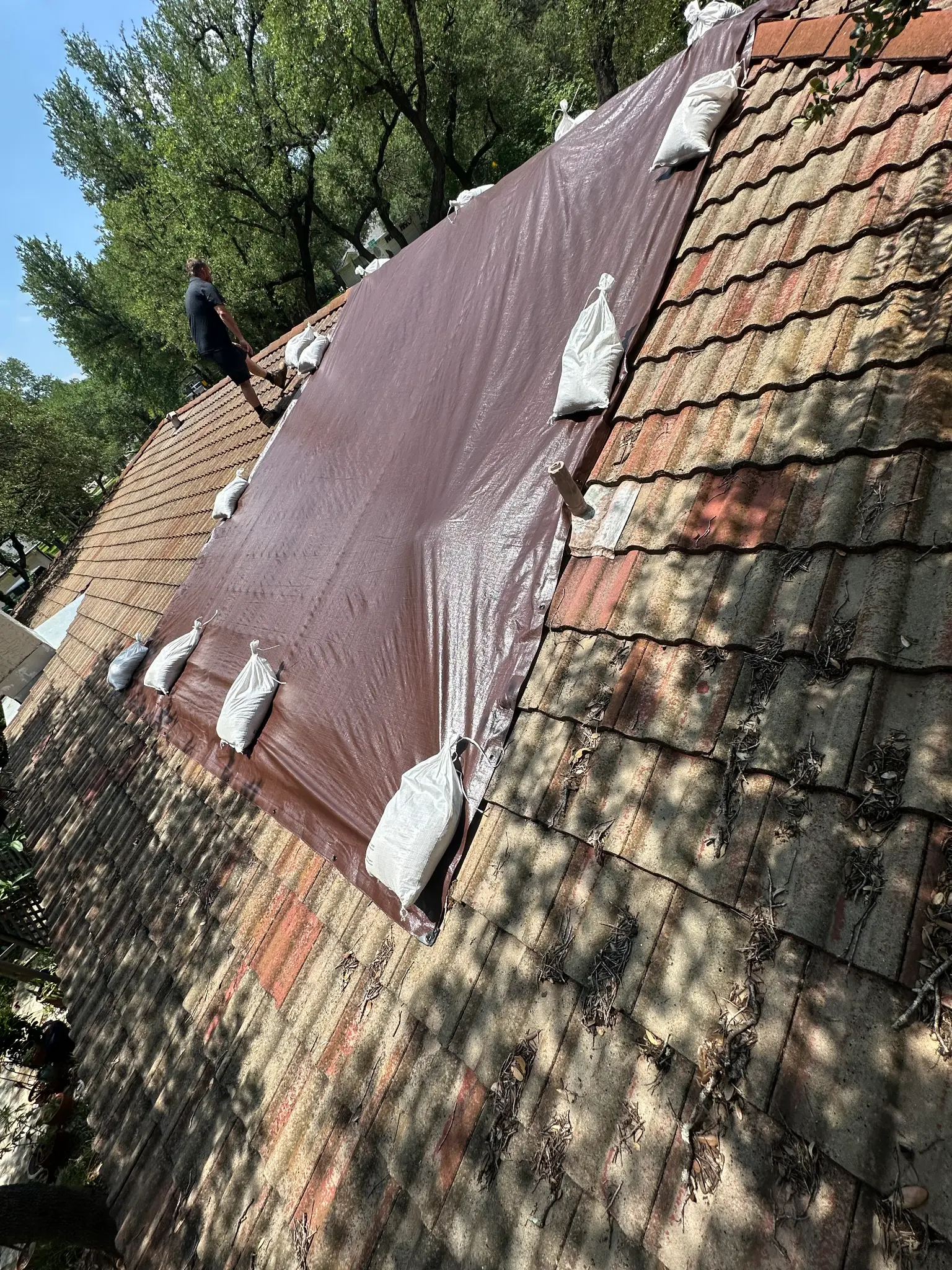 Brown emergency tarp secured with sandbags on a Texas tile roof