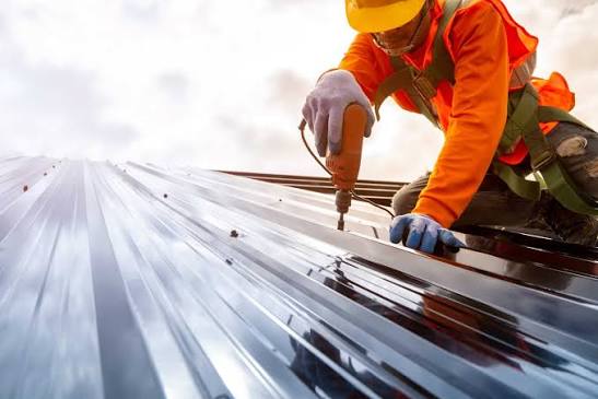 Commercial roofer in an orange safety vest and yellow hard hat installing metal roofing panels