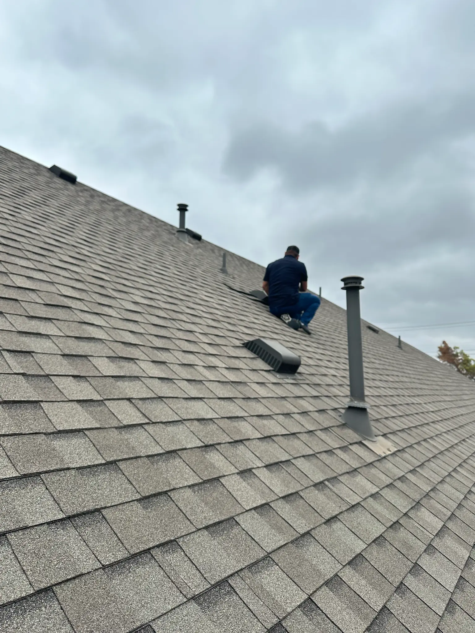 Finished gray shingle roof with a Roof Royale crew member completing quality repair work